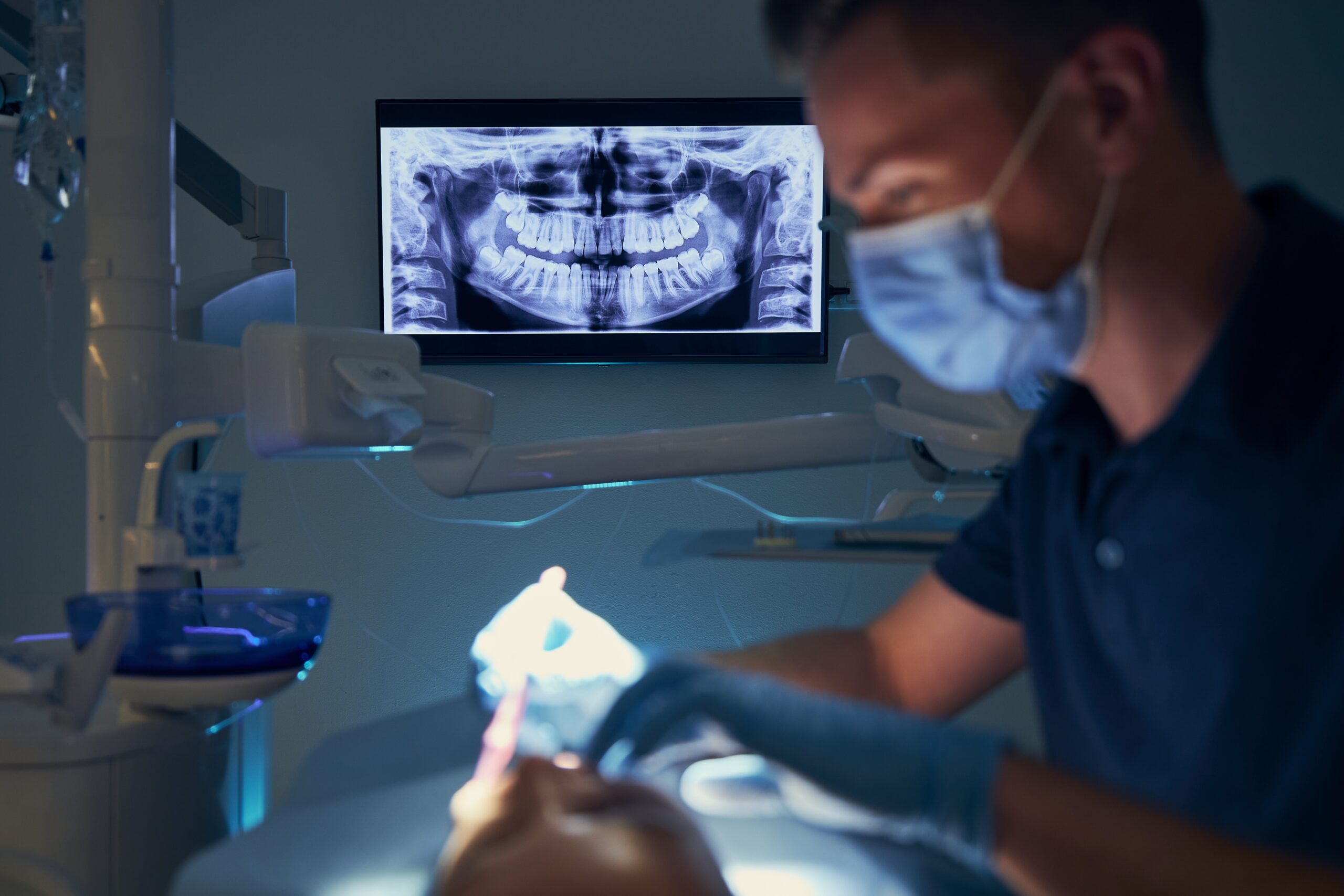 Dentist examining patient with dental equipments against modern dental surgery with x-ray.