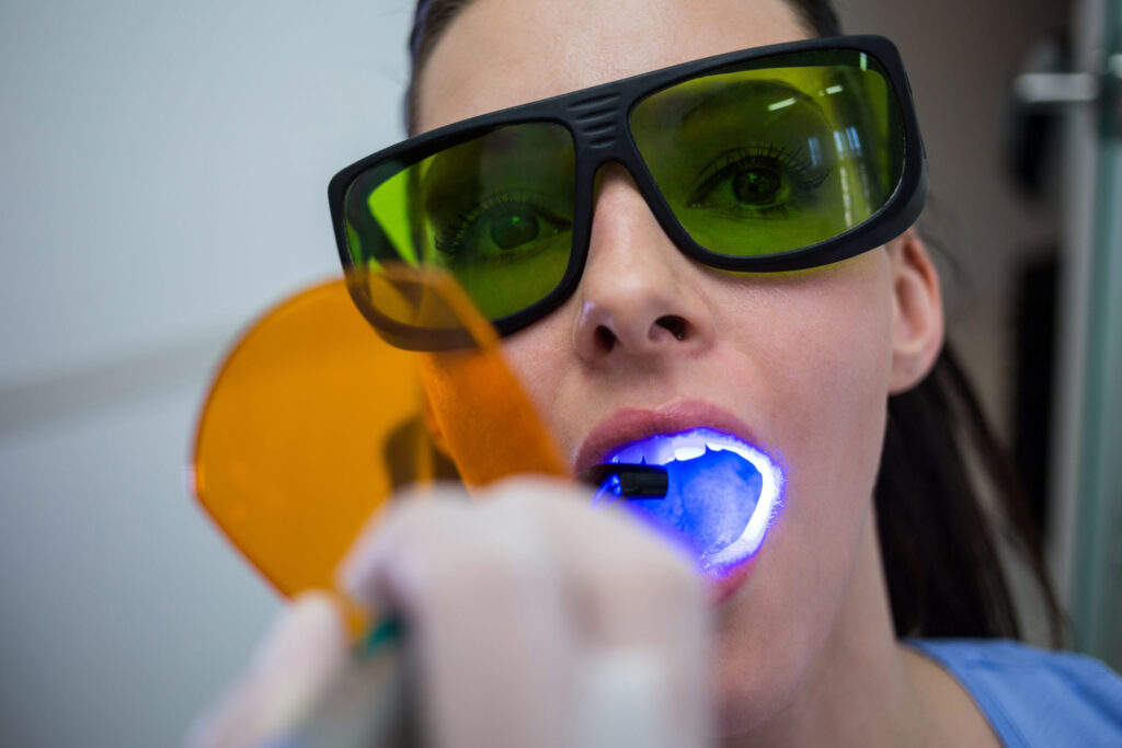 Dentist examining patients teeth with dental curing light at clinic