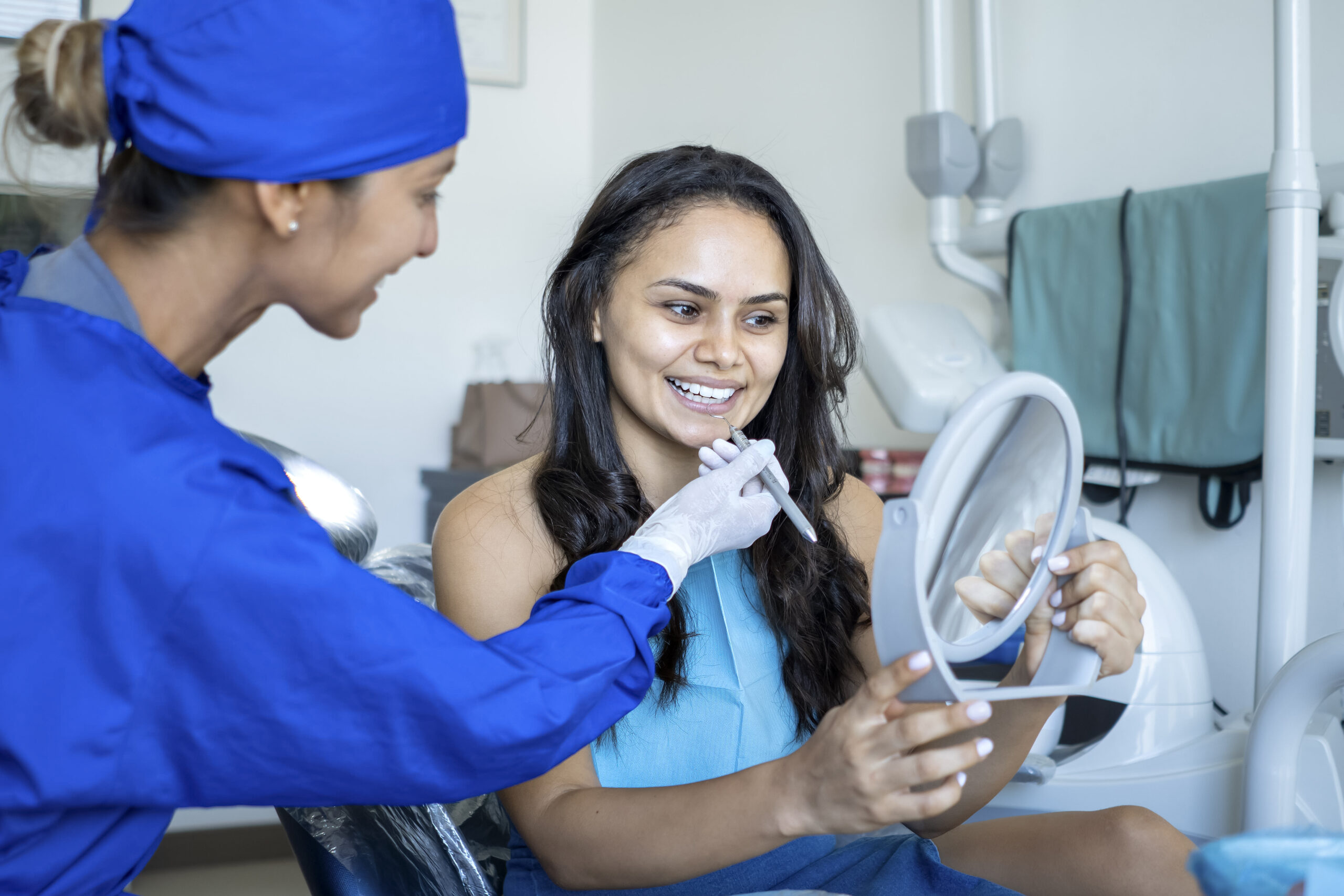 A patient smiles and looks into a mirror while being seen by the dentist.